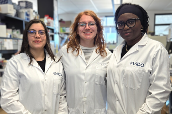 three women in lab coats smiling at camera